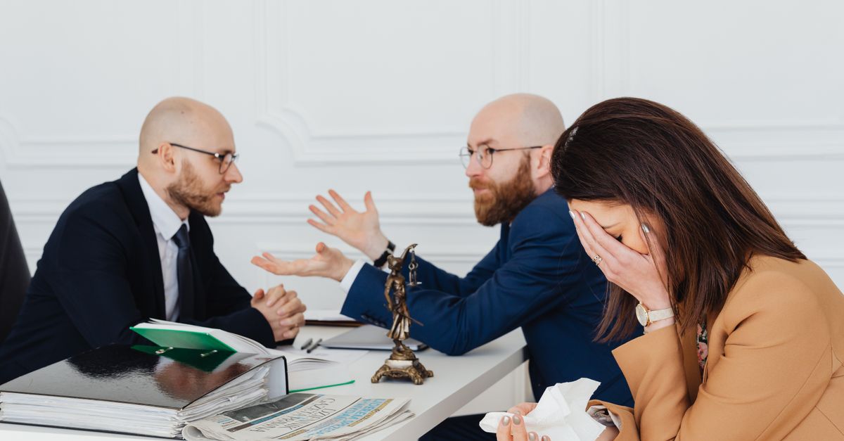 A lawyer mediates an emotional settlement discussion with a distressed couple in a legal office.
